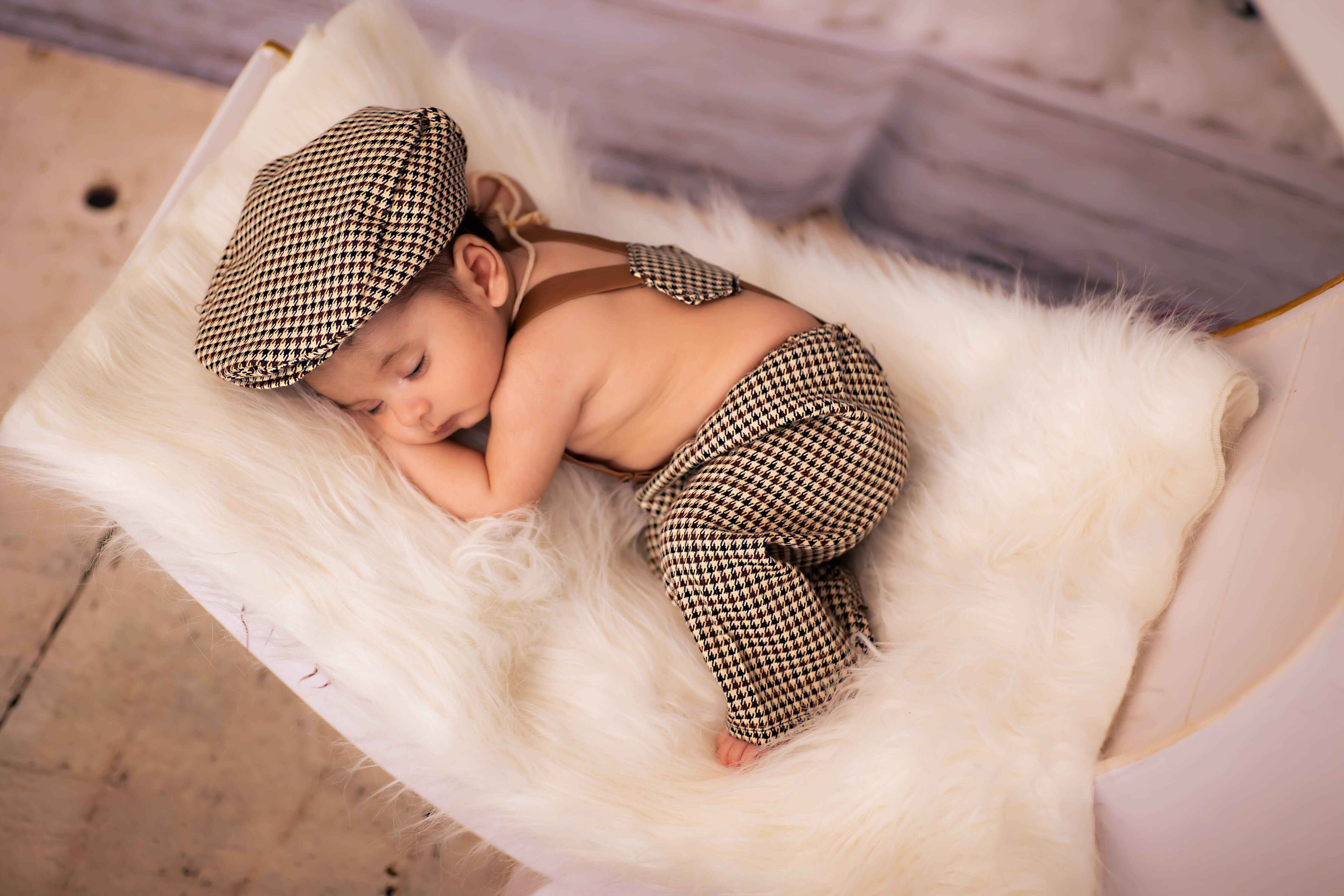 Baby in formal attire, peacefully resting on a soft white fur pillow, creating a charming baby photoshoot moment.